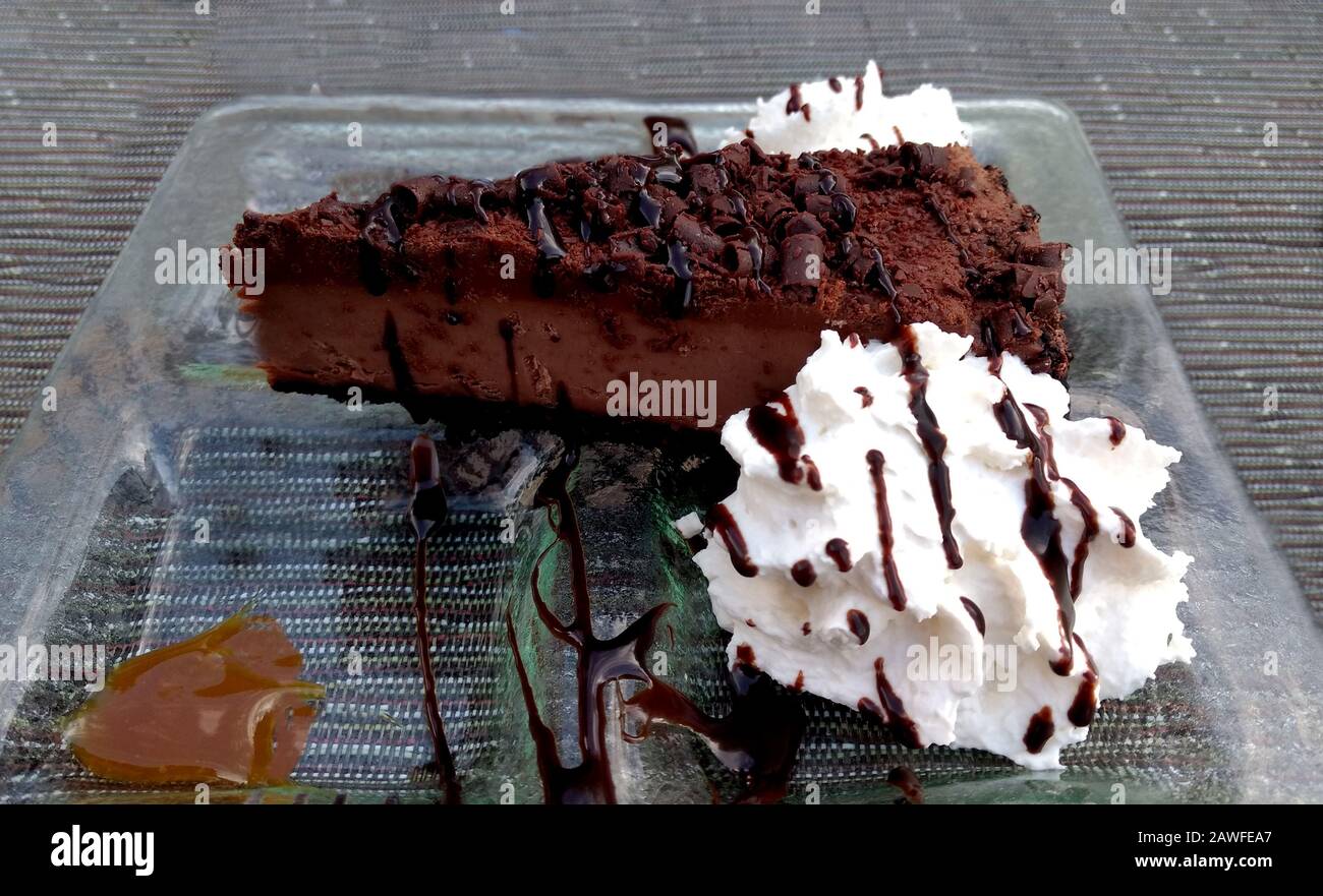 Una ricca fetta di torta al cioccolato fondente, decorata con nastri di salsa al cioccolato e guarnita con caramello e panna montata Foto Stock