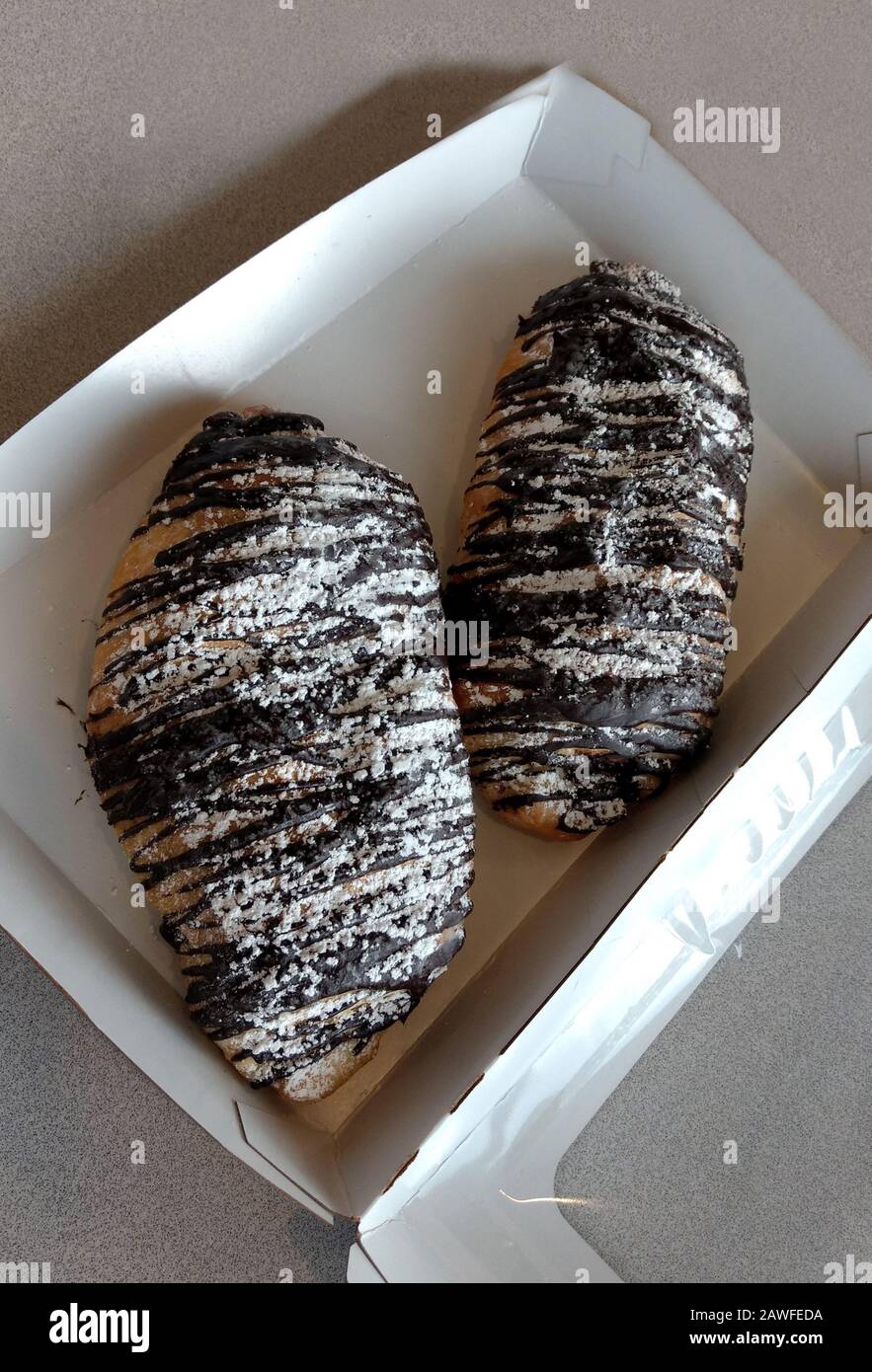 Due croissant al cioccolato sono in una scatola da togliere, conditi con cioccolato fuso, spolverati con zucchero alimentato e pronti a condividere Foto Stock