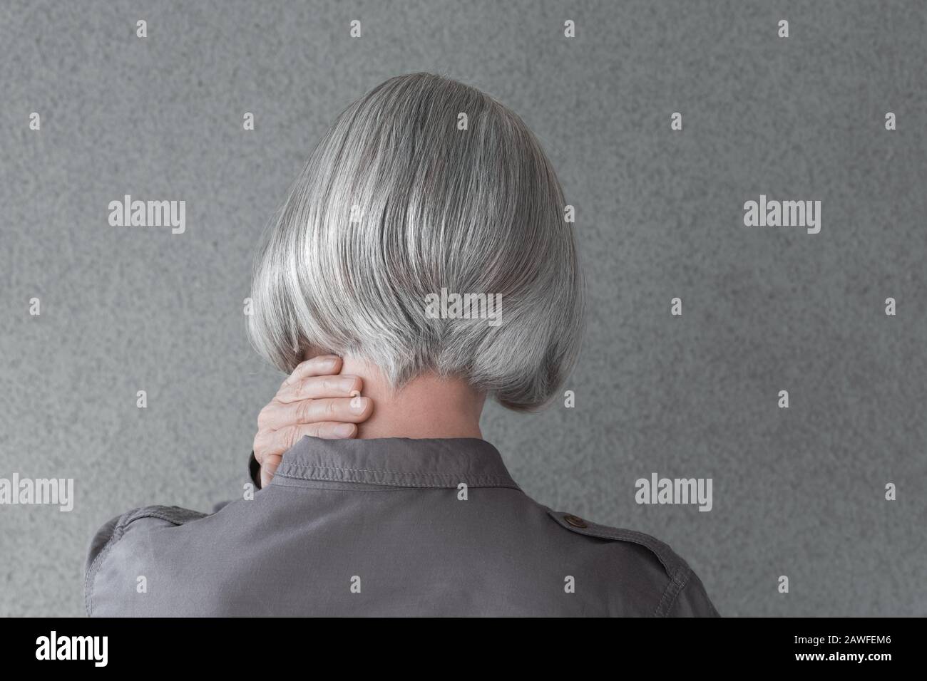 Donna con capelli grigio argento, tenendo la mano sul collo, da dietro. Foto Stock