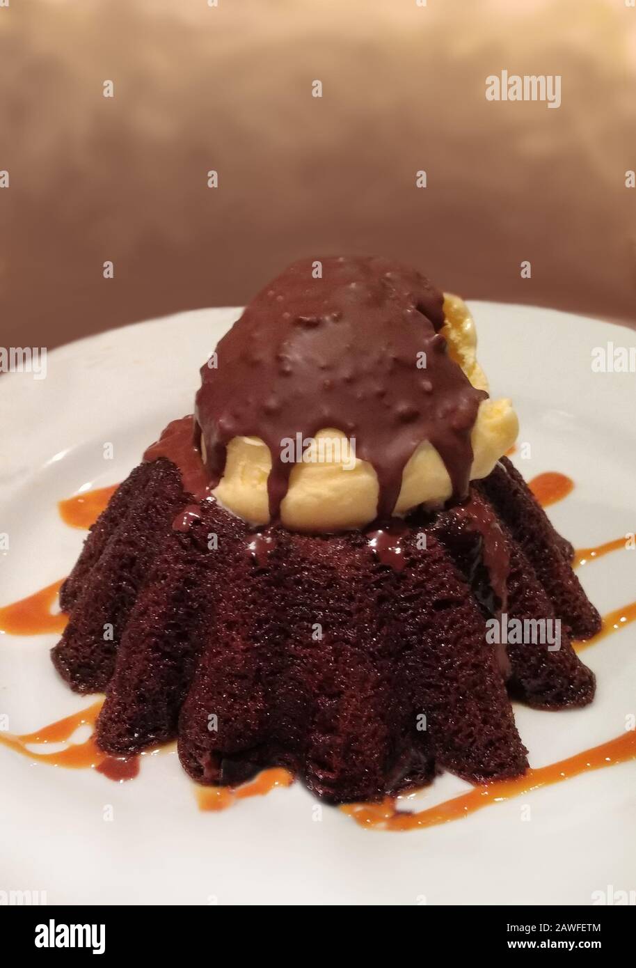 Una torta di lava al cioccolato caldo, si siede su un nastro di caramello ed è sormontata da una paletta di gelato alla vaniglia e una conchiglia di cioccolato duro Foto Stock