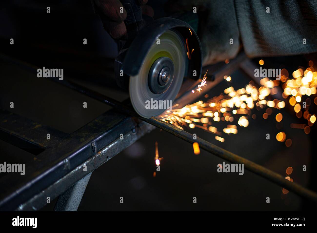 Lavorazione del metallo in officina. Rettifica del metallo. L'operatore realizza la struttura di un profilo metallico. Creazione di uno scaffale per l'abitante della città. Scintille Foto Stock