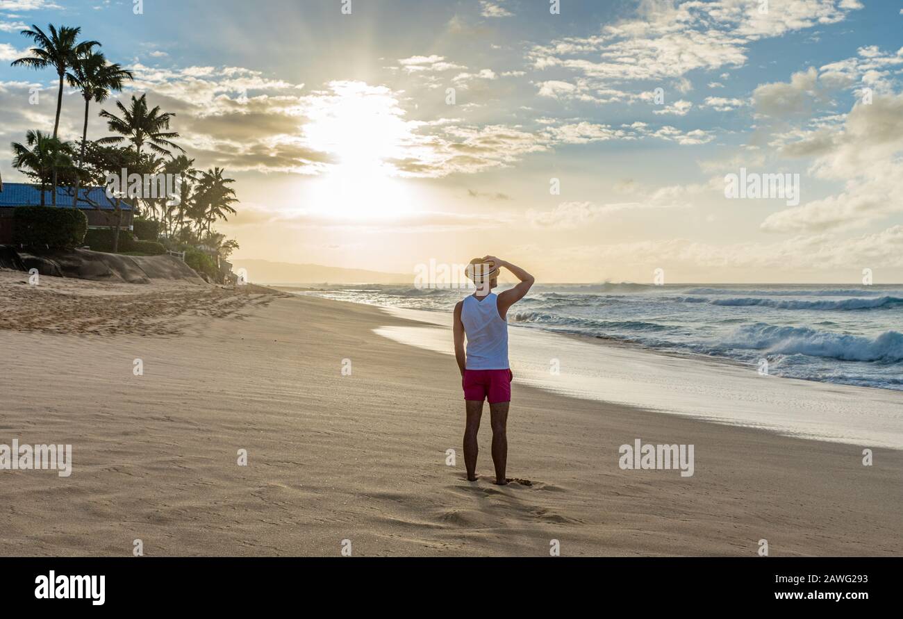 Giovane maschio caucasico in piedi su Sunset Beach in Hawaii al tramonto guardando verso l'oceano Foto Stock