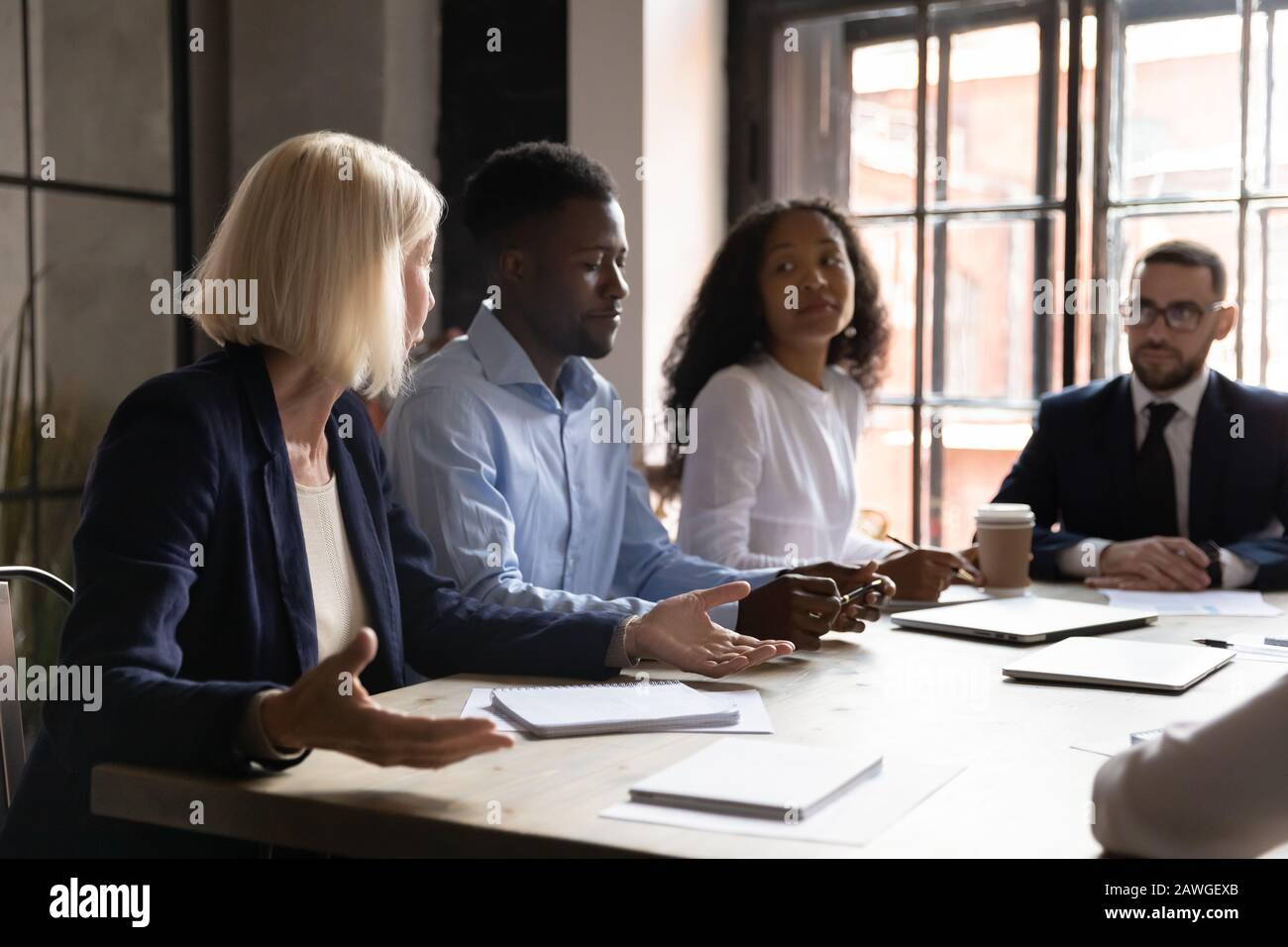 Team diversificato che ascolta leader anziani durante una riunione di gruppo in sala riunioni Foto Stock