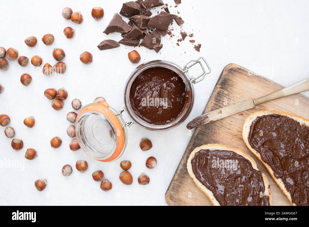 Cioccolato alla nocciola vegano fatto in casa spalmato su pane di pasta acida e in un recipiente di fornace, con nocciole non sgusciate e pezzetti di cioccolato fondente Foto Stock