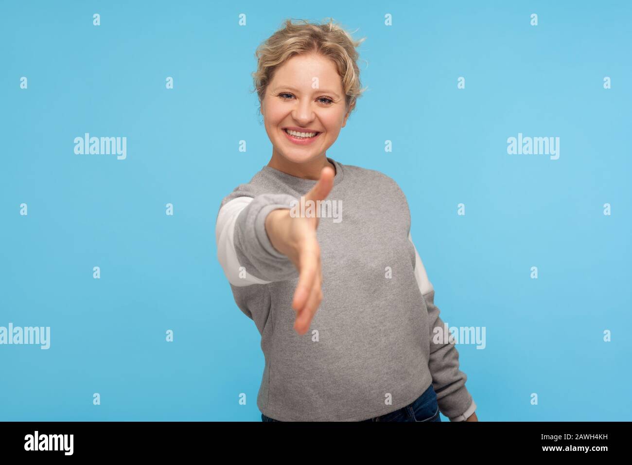 Piacere di conoscarvi! Donna ospitale con capelli corti in felpa casual sorridente amichevole alla macchina fotografica e dare mano a handshake, fiducia e accordo. Foto Stock