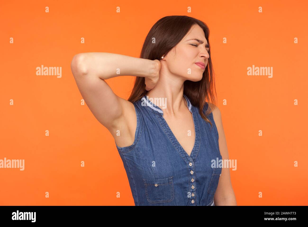 Collo ferente. Donna bruna malsana in denim vestito in piedi massaggiando il collo e la sporcizia nel dolore, la tensione muscolare sofferenza, la spina dorsale ferita. Foto Stock