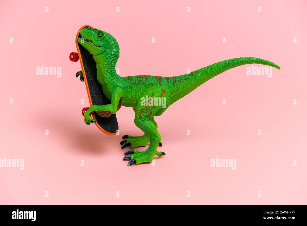 carino dinosauro verde con skate isolato su uno sfondo rosa Foto Stock