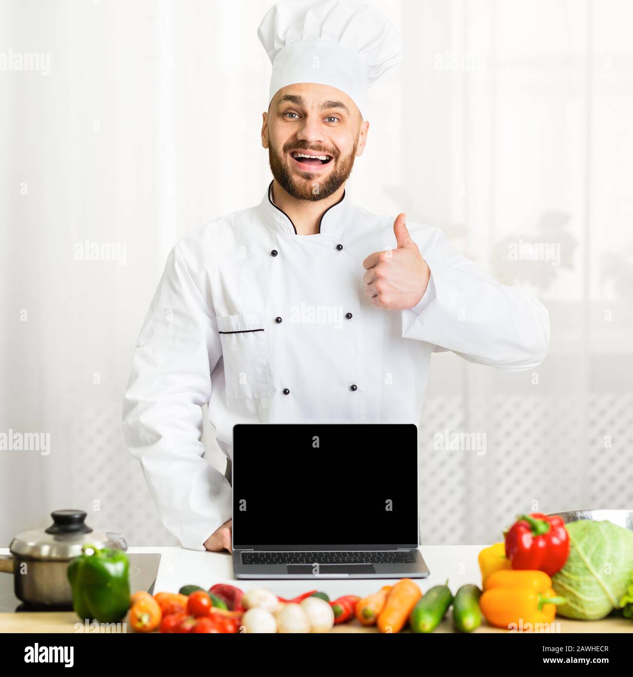 Chef Guy Holding Laptop Gesturing Thumbs-Up Standing In Cucina Foto Stock