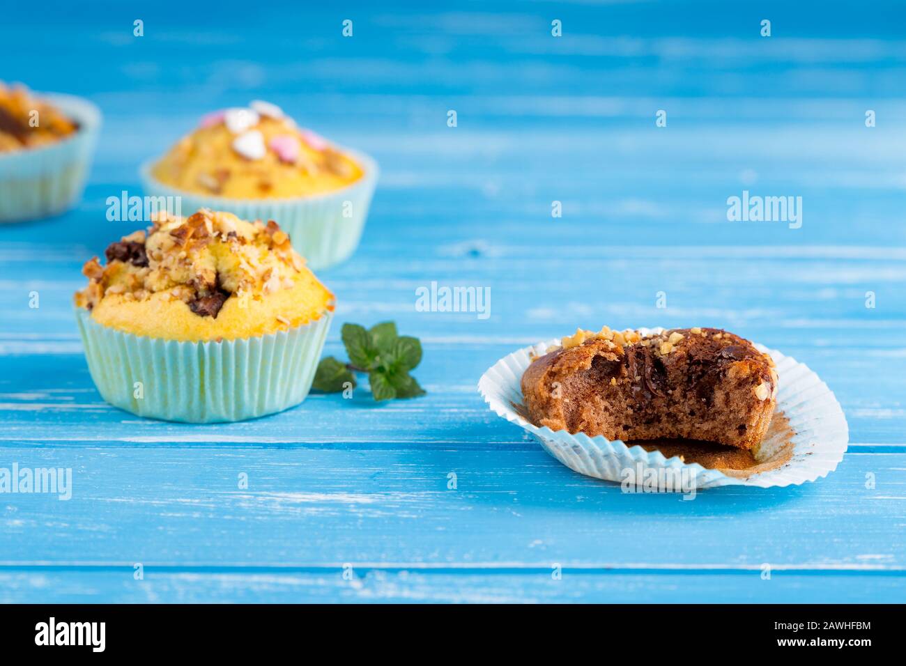 Morso il muffin con i dadi e il cioccolato sul supporto per cupcake di carta. Sfondo rustico in legno blu. Foto Stock