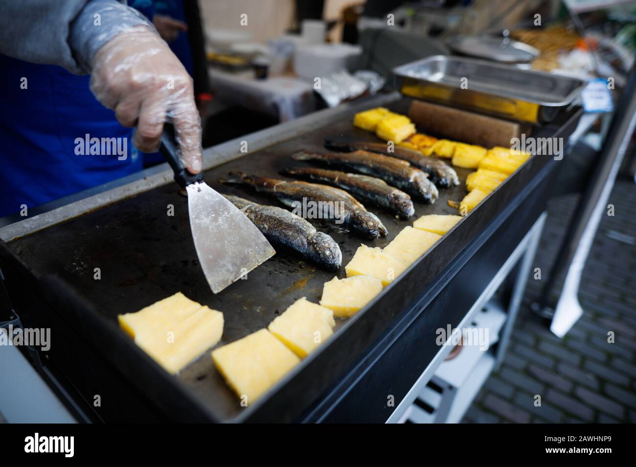Profondità di campo poco profonda (fuoco selettivo) immagine con un uomo che cucina trote pesce e polenta su una stufa all'aperto in una giornata fredda. Foto Stock