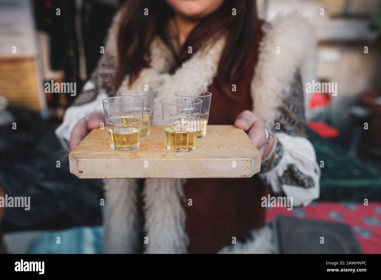 Profondità di campo poco profonda (fuoco selettivo) immagine con una donna che tiene un piatto di legno con palinca (o tuica), tradizionale prum brandy romeno. Foto Stock