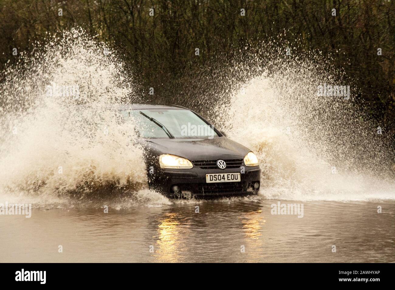 Un'auto che passa attraverso acque profonde e inondate a velocità elevata, gettando spray su una strada a Kirkham, nel Lancashire, Regno Unito. Feb, 2020. Tempo del Regno Unito; Storm Ciara strade inondato a Kirkham. Credit: MediaWorldImages/Alamy Live News Foto Stock