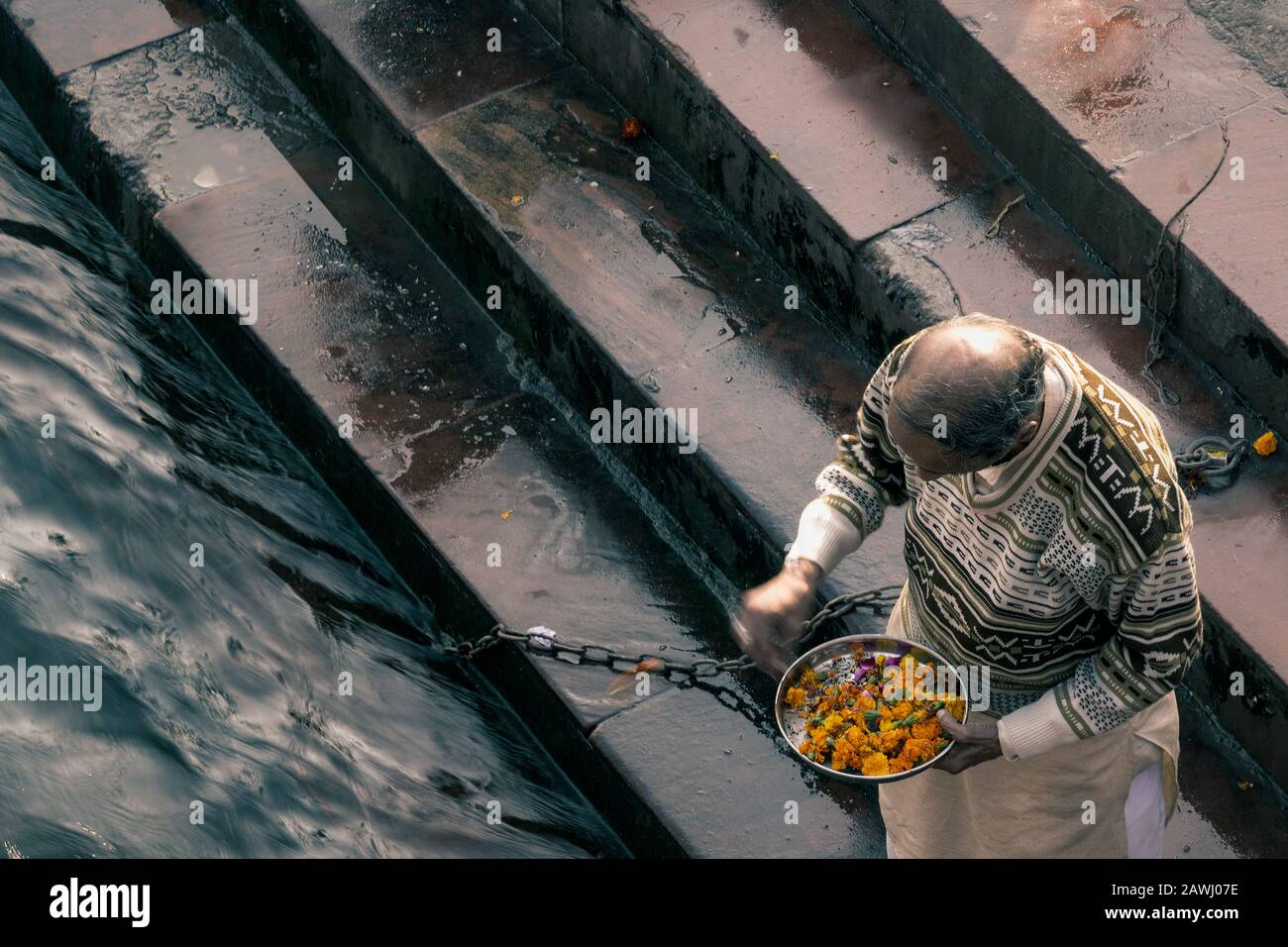 Un vecchio uomo che getta fiori nel fiume Ganga Foto Stock