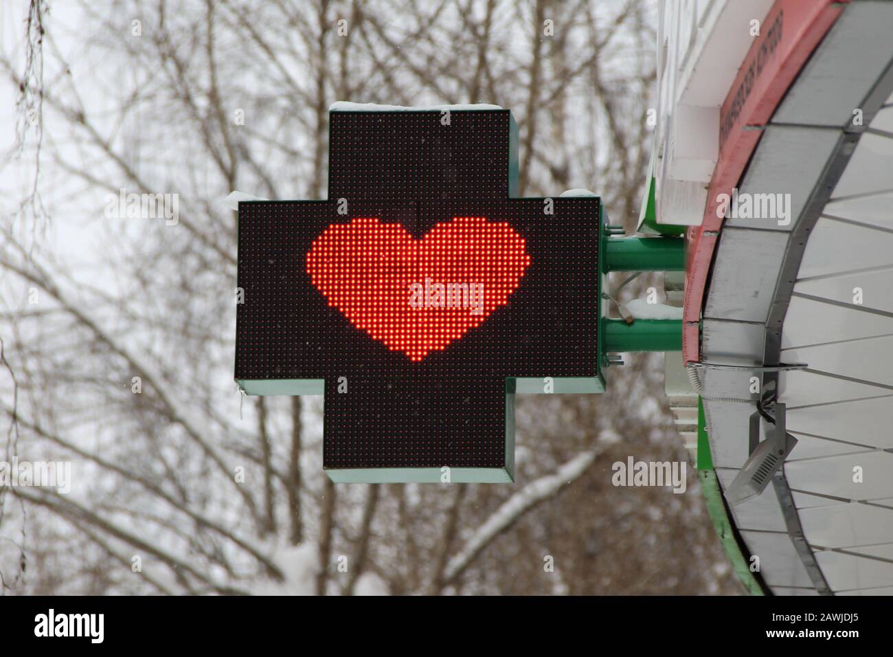 Cuore rosso su un pannello luminoso sotto forma di croce. Pubblicità disegno di una farmacia su una strada della città. Foto Stock