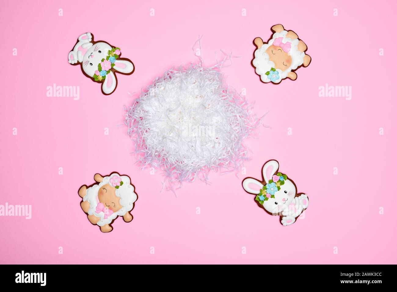 Vista dall'alto di biscotti smaltati isolati su sfondo rosa. Biscotti allo zenzero di Pasqua in forma di due coniglietti in wreaths e due pecore intorno al nido bianco. Concetto di vacanze di primavera e pasqua. Foto Stock
