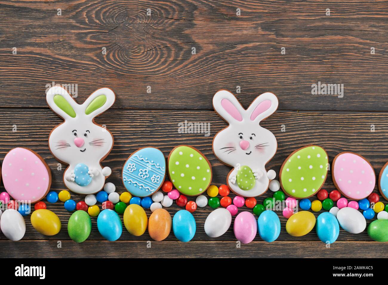 Da sopra vista di grandi e piccole palline di cioccolato alle arachidi in guscio di zucchero croccante isolato su sfondo di legno. Primo piano di biscotti patinati allo zenzero di pasqua a forma di due coniglietti e uova in fila. Foto Stock