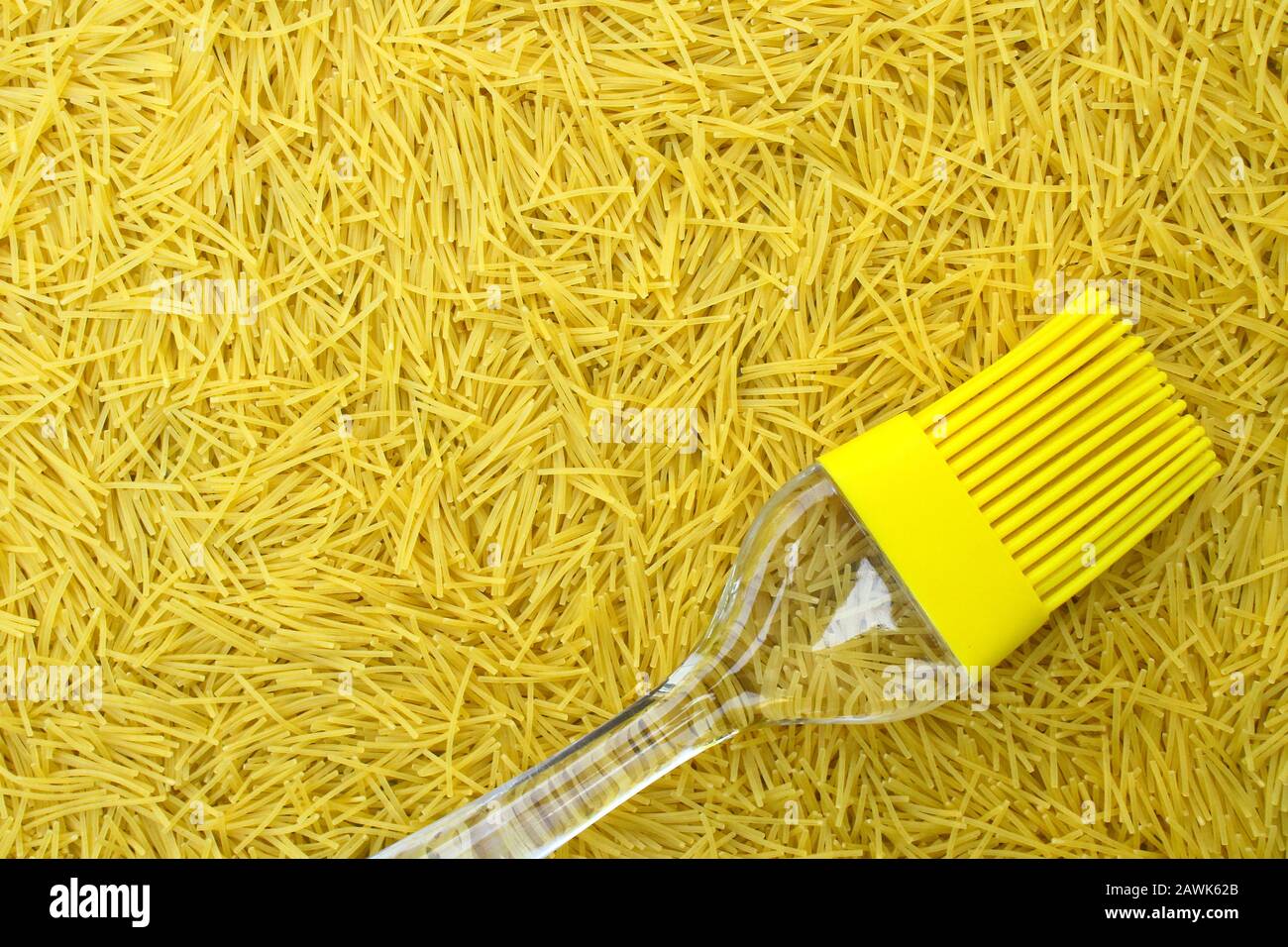 sfondo con pasta italiana vermicelli e pennello da cucina in silicone giallo o tassel con manico trasparente, spazio di copia per elementi di testo e design Foto Stock