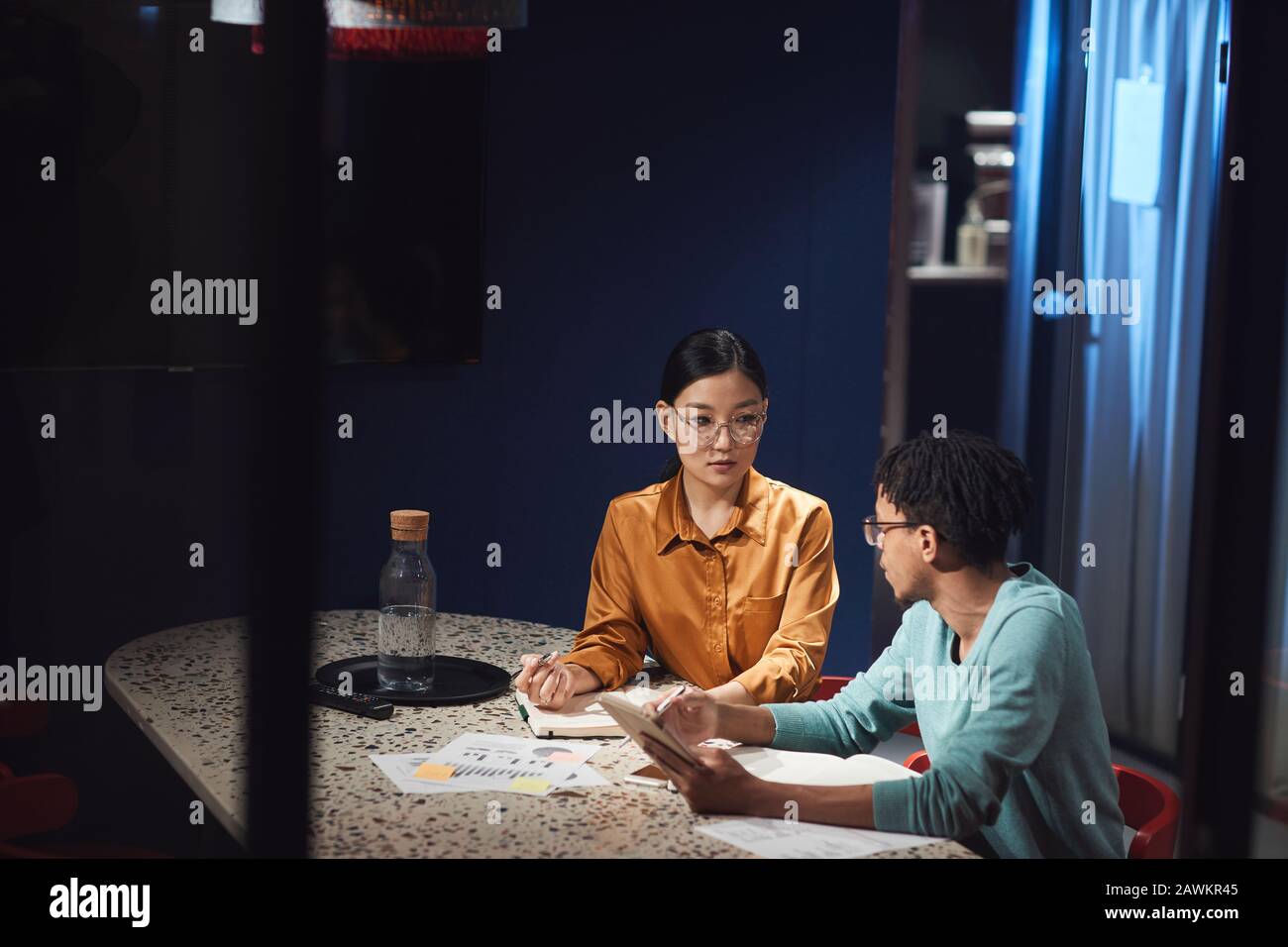Ritratto di businesswoman asiatico che parla con collega mentre lavora in ritardo in ufficio scuro, spazio poliziotto Foto Stock