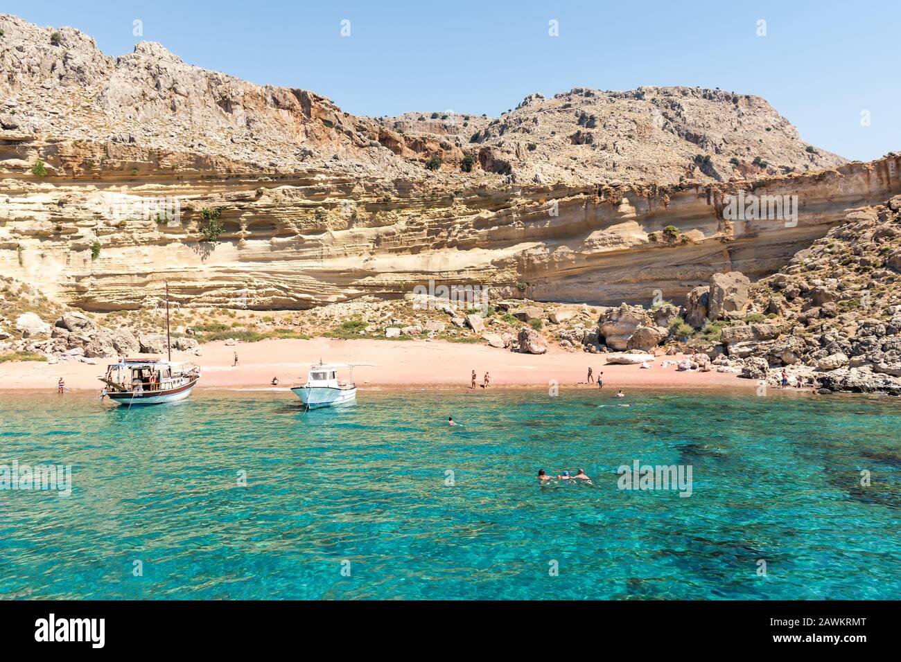 Barche turistiche ancorate dalla spiaggia di sabbia rossa, la gente ha divertimento (Rodi, Grecia) Foto Stock
