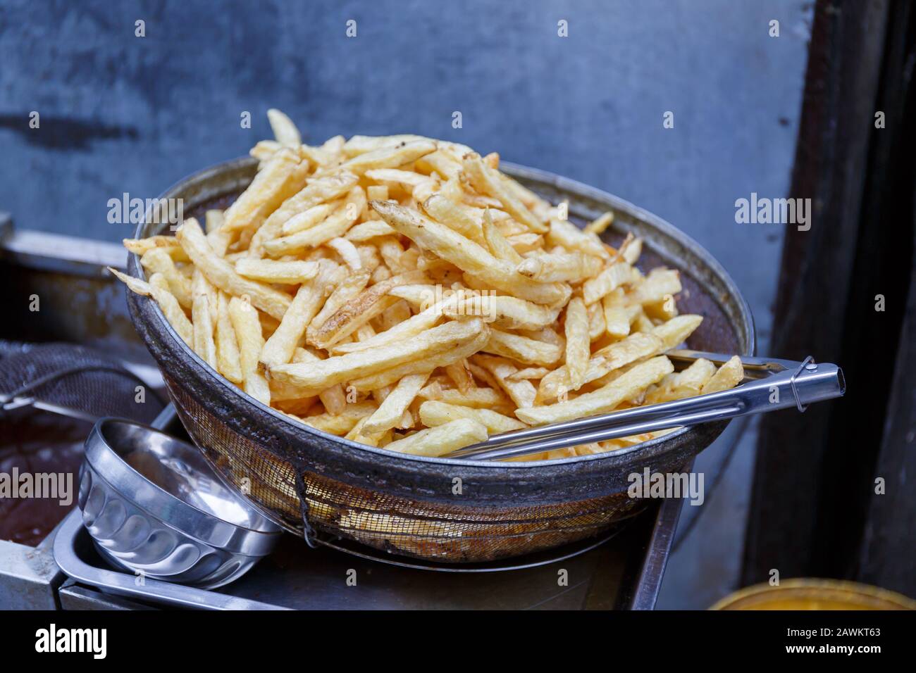 Vista sulle patatine fritte fatte in casa e fritte fresche/cotte in una ciotola di metallo con tong di cibo. Spuntino delizioso, croccante e croccante. Foto Stock