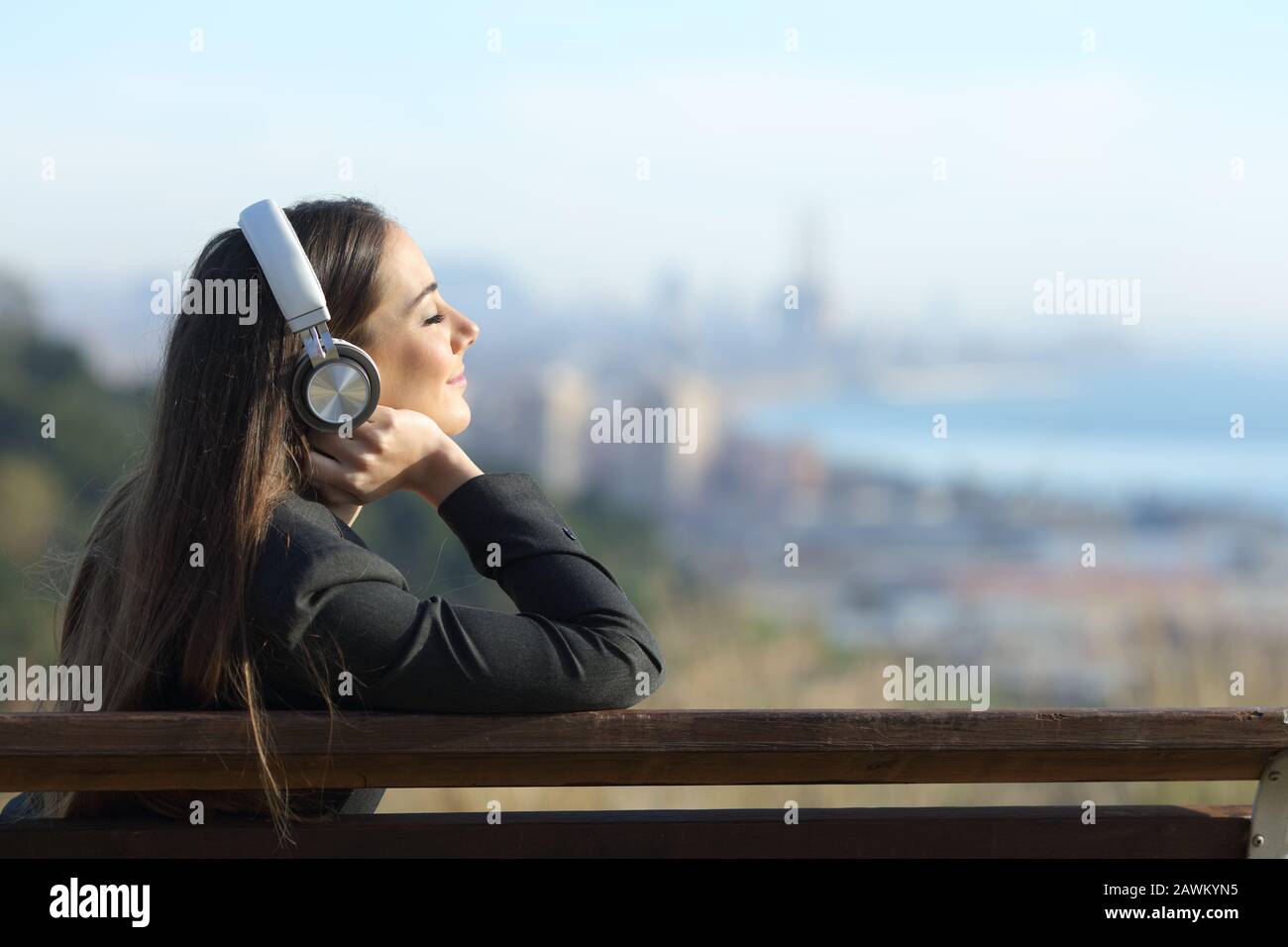Donna d'affari rilassante ascolto di musica indossando cuffie seduti su un banch all'aperto Foto Stock