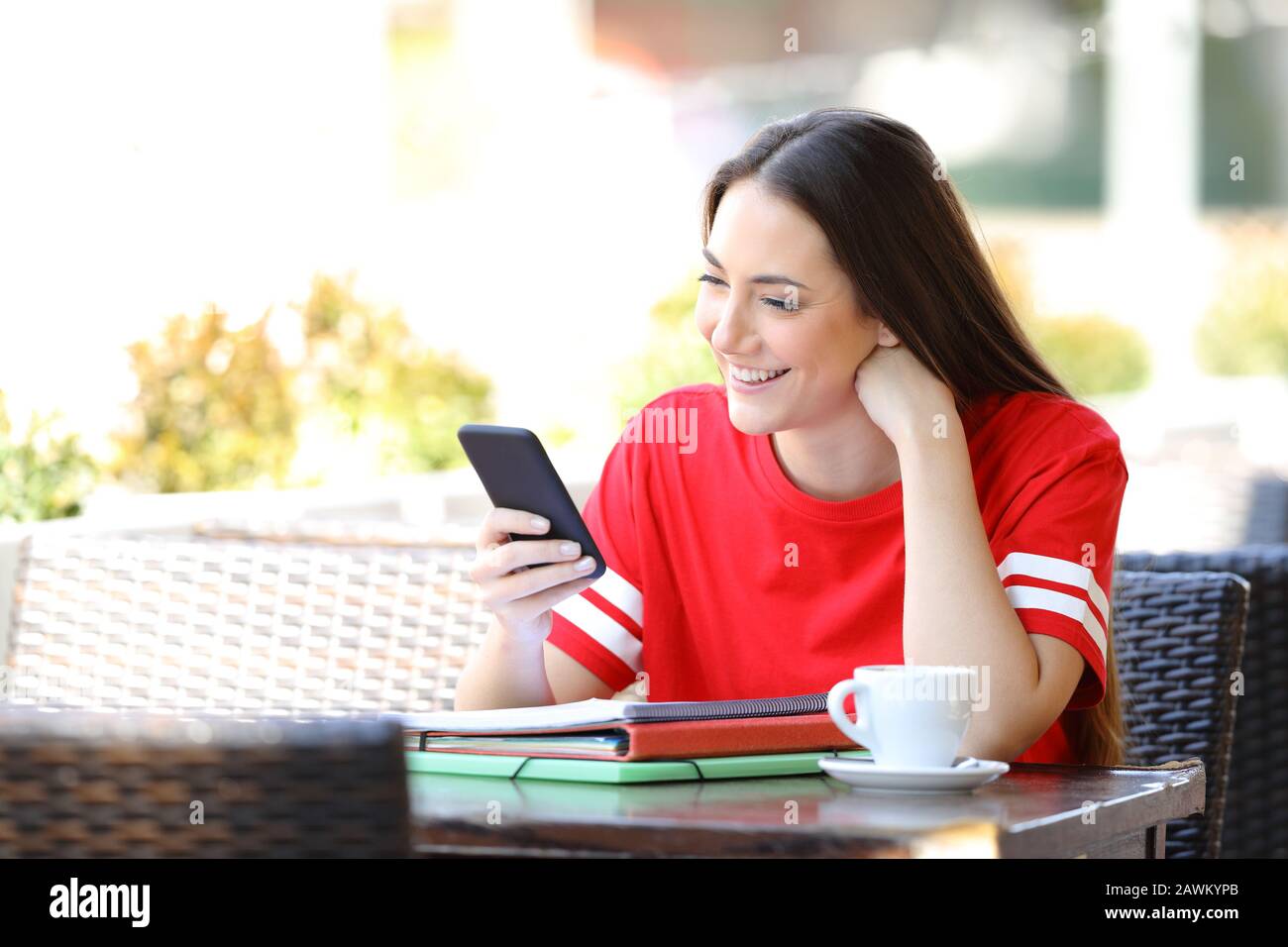 Buon studente che legge i contenuti di smartphone seduti in una terrazza della caffetteria Foto Stock