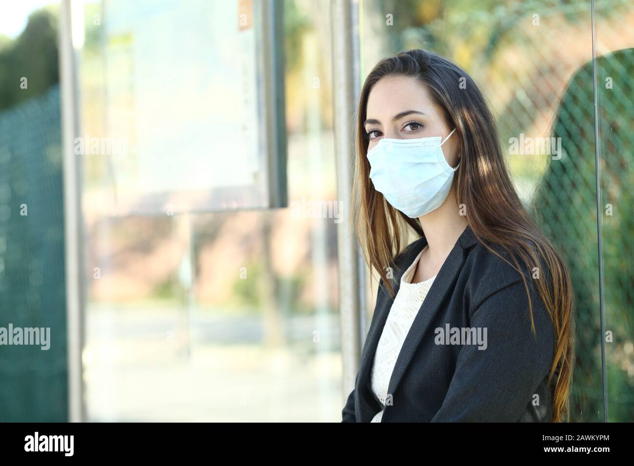 Donna che indossa una maschera per prevenire il contagio seduto in un bus stop in attesa di trasporto Foto Stock