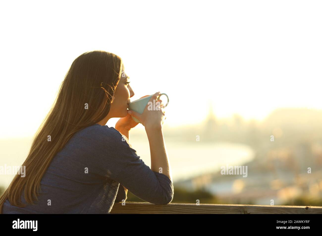 La ragazza felice beve caffè contemplando le viste da un balcone al tramonto Foto Stock