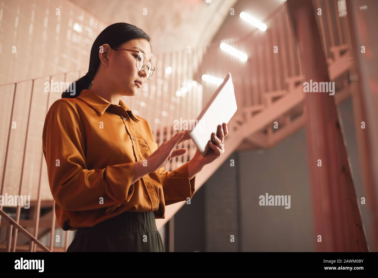 Ritratto della giovane donna d'affari asiatica usando un tablet mentre si alza per le scale all'aperto, copia spazio Foto Stock