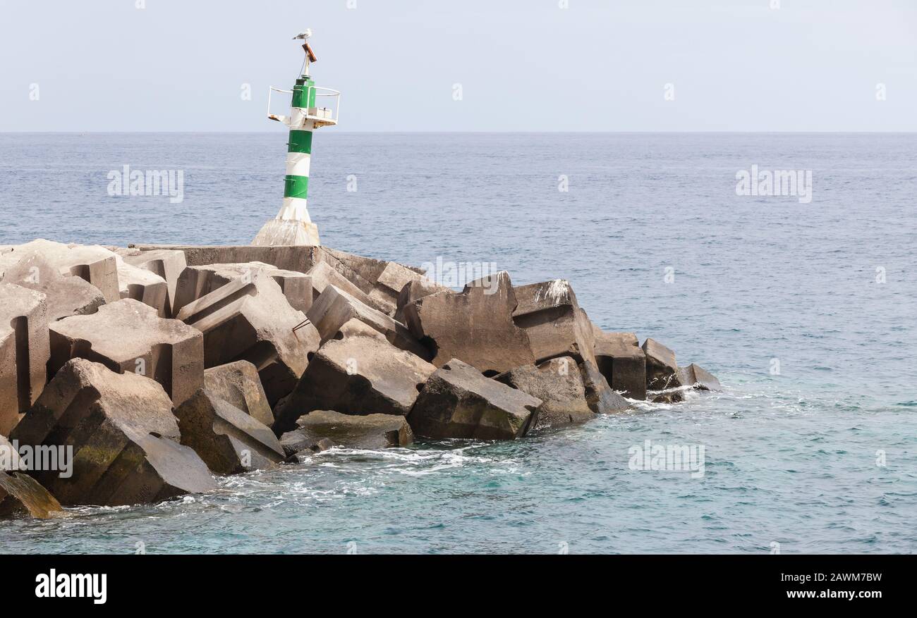 Torre faro a strisce verdi e bianche che si erge sul frangiflutti d'ingresso di Marina da Calheta. Madeira, Portogallo Foto Stock