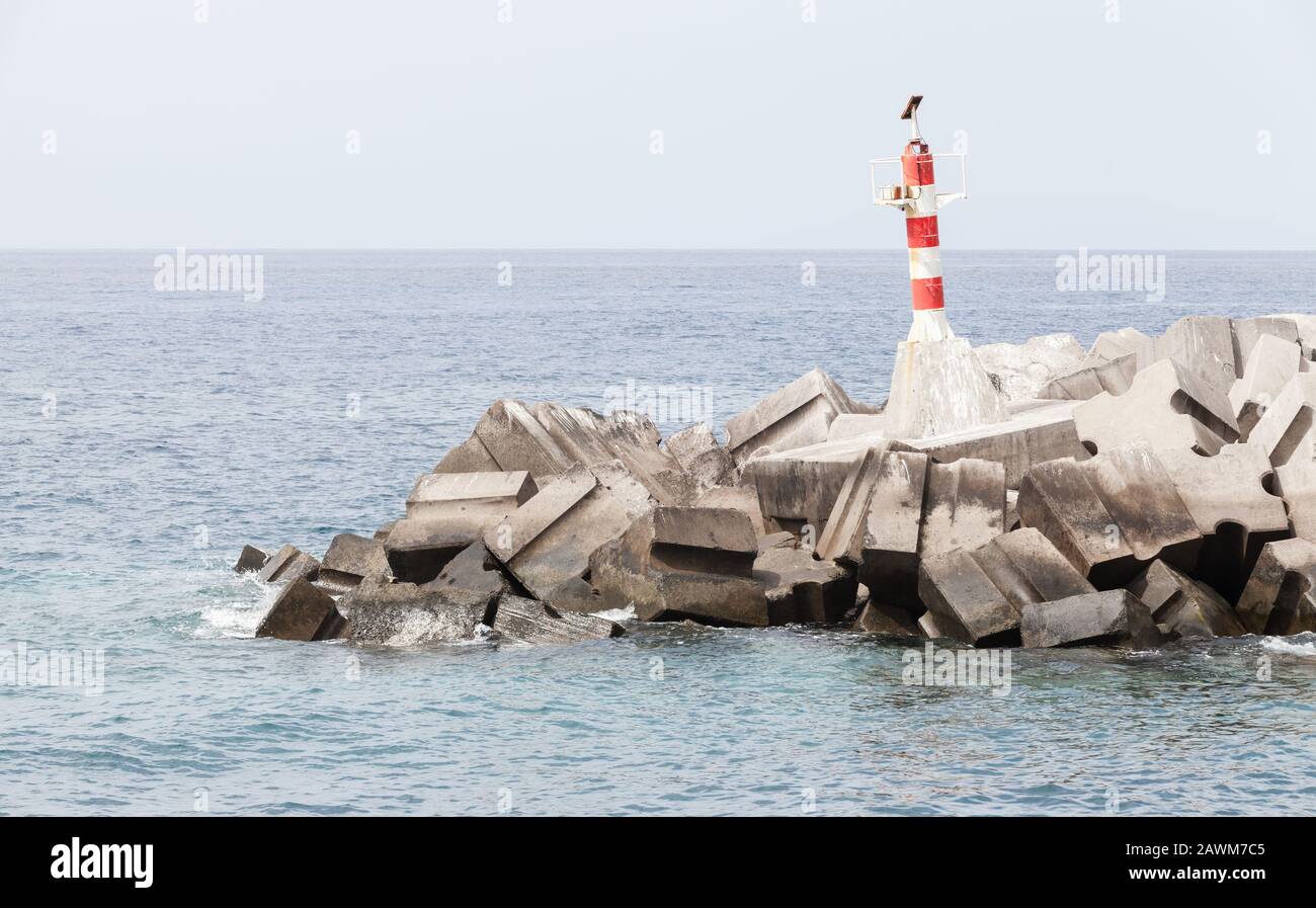 Torre faro a strisce rosse e bianche che si erge sul frangiflutti d'ingresso di Marina da Calheta. Madeira, Portogallo Foto Stock