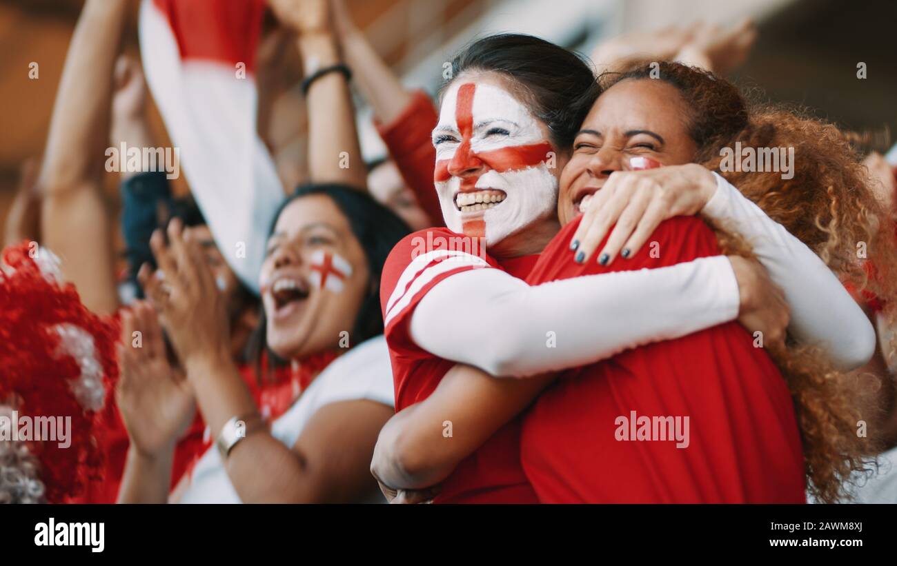 I tifosi di calcio inglesi femminili con la bandiera inglese dipinta sul loro volto abbracciandosi dopo la vittoria della loro squadra. Spettatori femminili inglesi a piedi Foto Stock