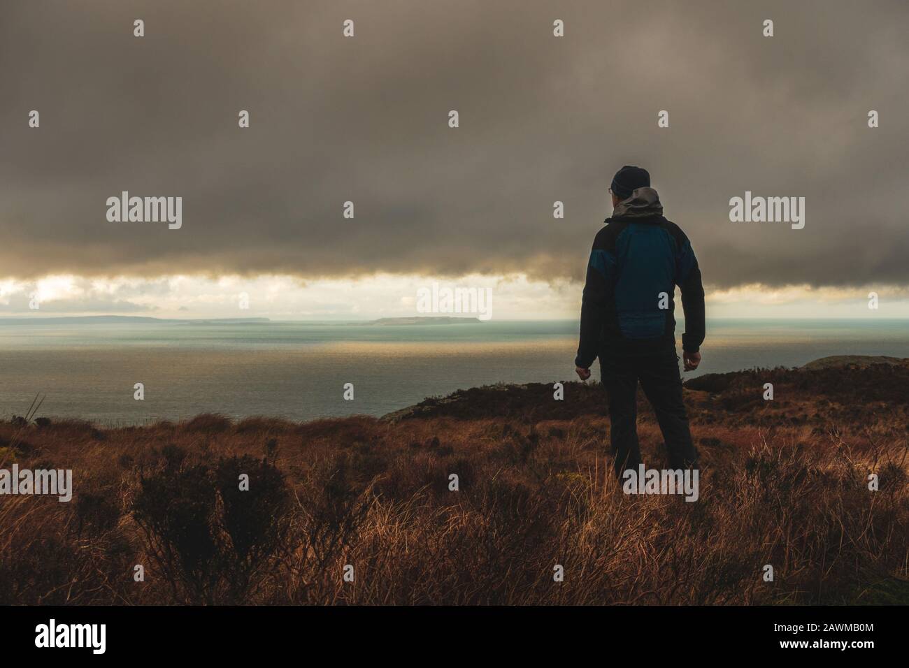 Persona che ammira il panorama dal Mull of Kintyre all'Irlanda del Nord e all'isola di Rathlin in condizioni meteorologiche estreme in inverno, Scozia, Regno Unito Foto Stock