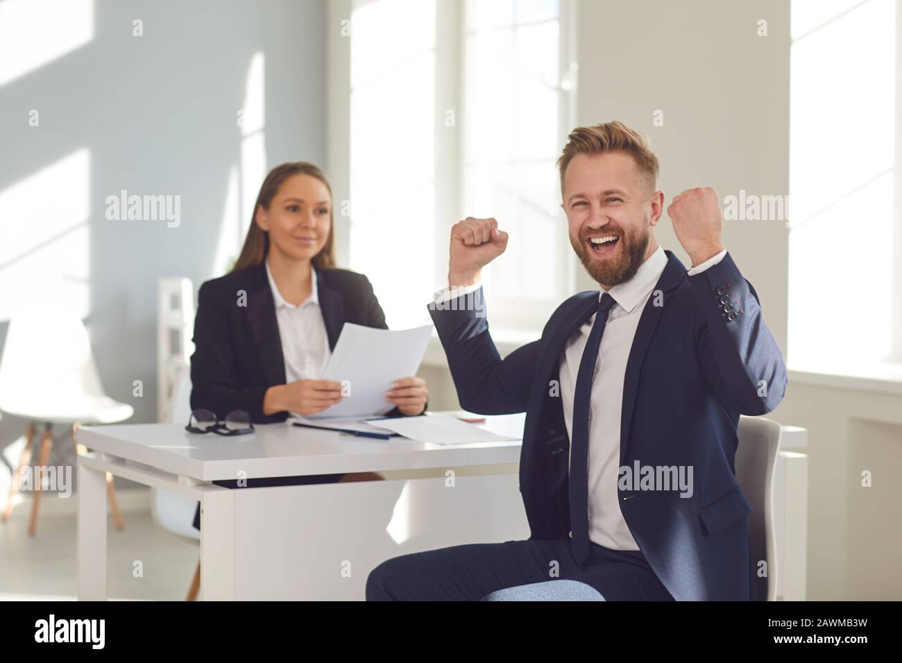 Intervista di successo. Un uomo in un vestito gioisce ad un nuovo lavoro seduto ad un tavolo con una donna datore di lavoro in un ufficio bianco. Foto Stock