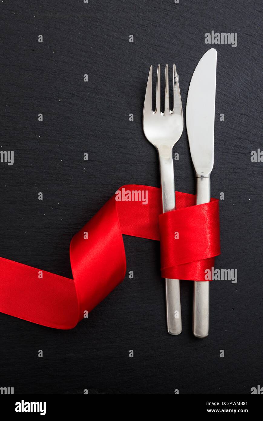Cena di San Valentino con tavolo. Posate a forchetta e coltello legate con nastro rosso passione su sfondo nero, vista dall'alto. Foto Stock