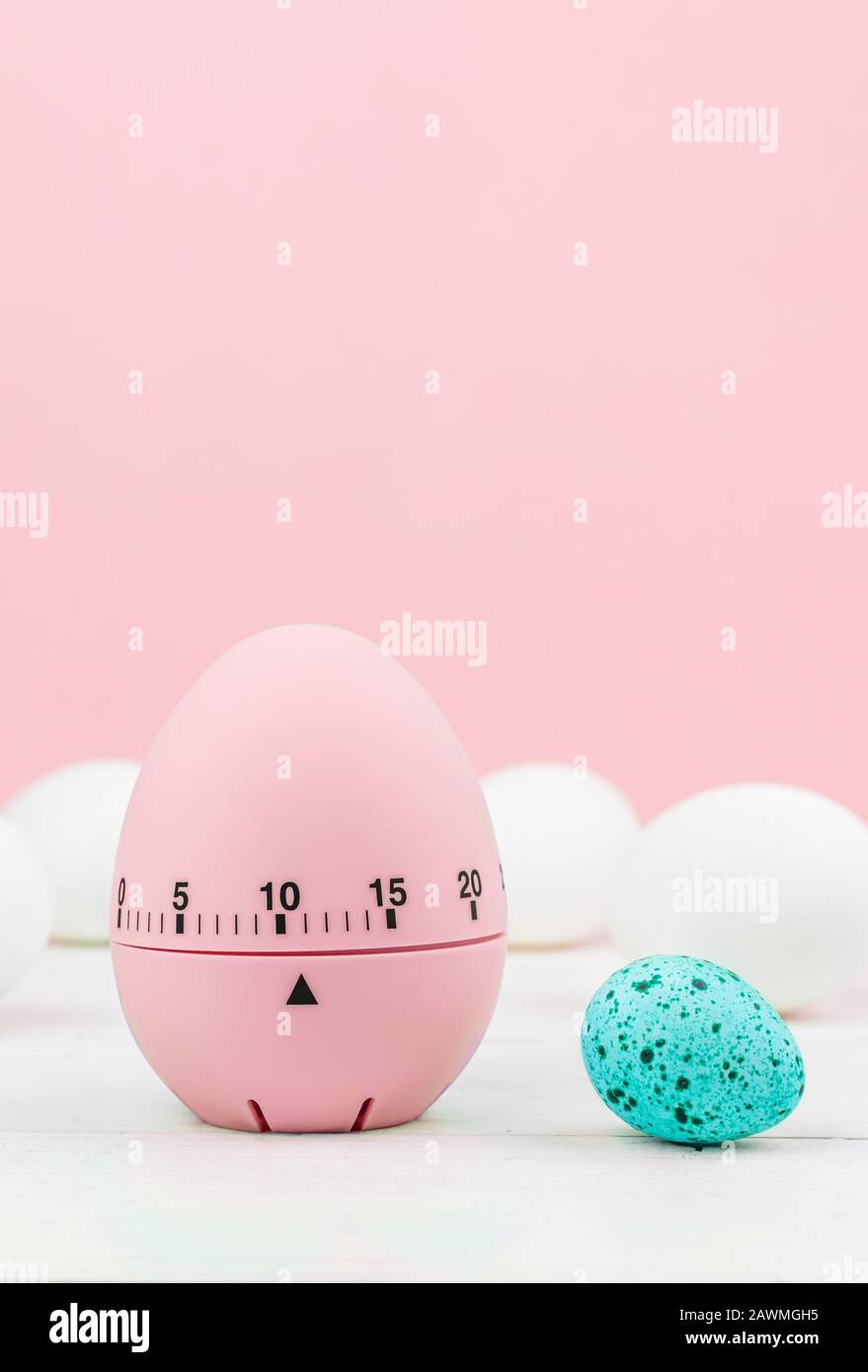 Cucina rosa uovo timer su sfondo rosa. Tempo di cottura, presto Pasqua. Uova di gallina bianca e uova di quaglia blu. Copia spazio Foto Stock