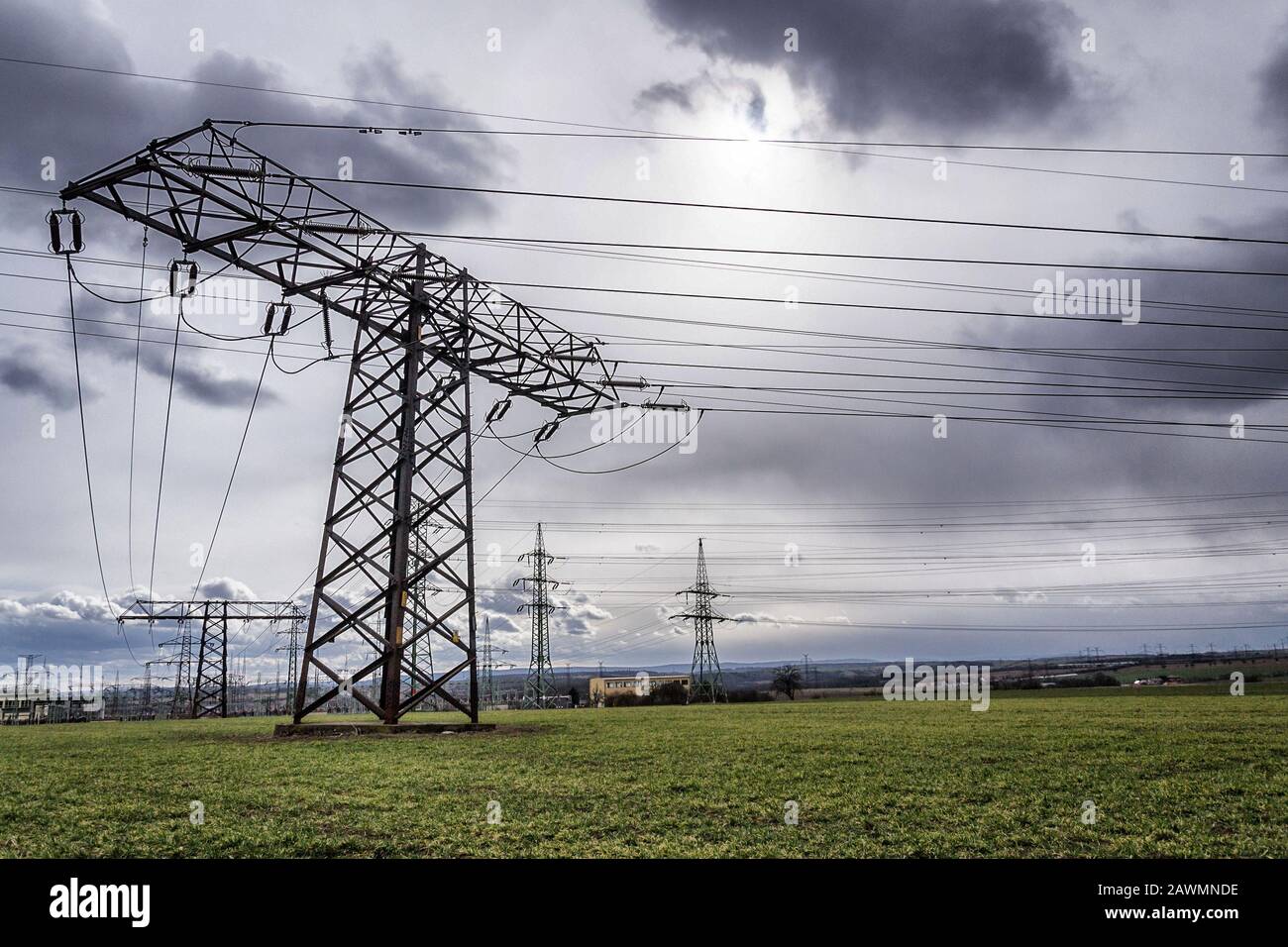 Sole nascosto dietro nuvole drammatiche e piloni di elettricità che conducono corrente dalla centrale di distribuzione, energia solare rinnovabile e stabilità della rete Foto Stock