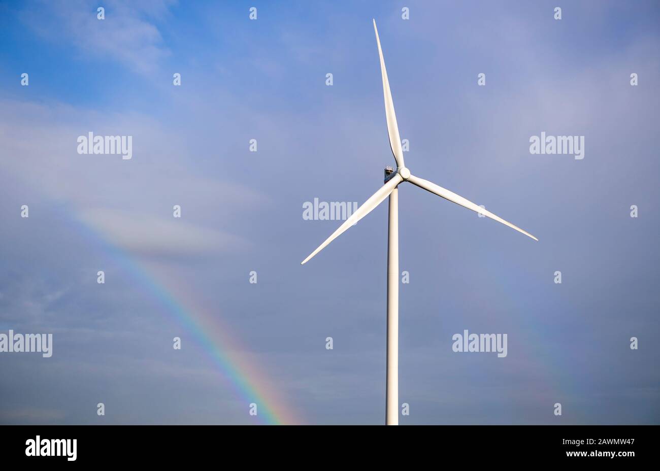 Turbina eolica singola contro un cielo blu con un arcobaleno sullo sfondo Foto Stock