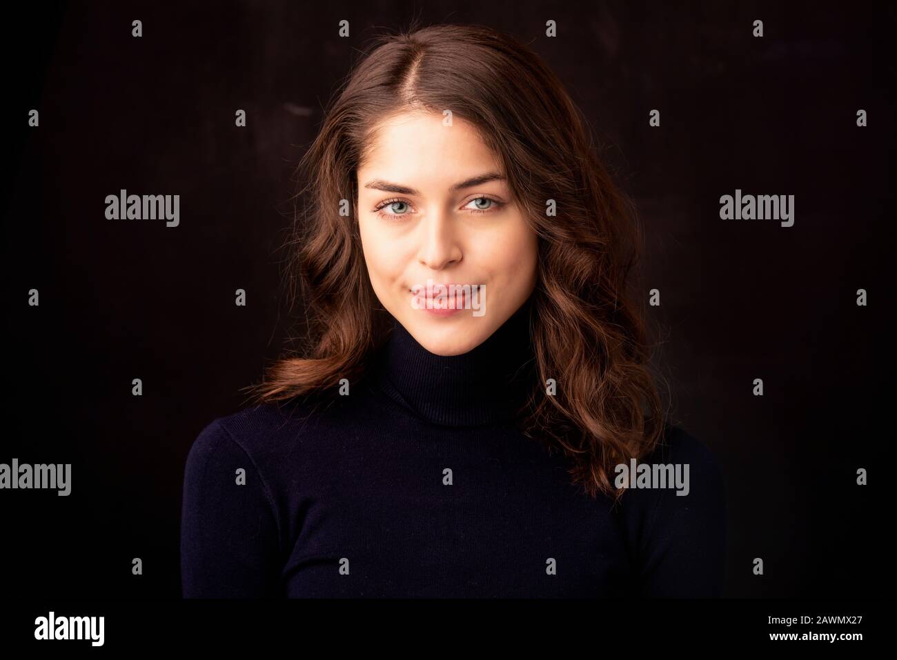 Primo piano portait di attraente giovane donna con bel sorriso che posa su sfondo scuro. Foto Stock