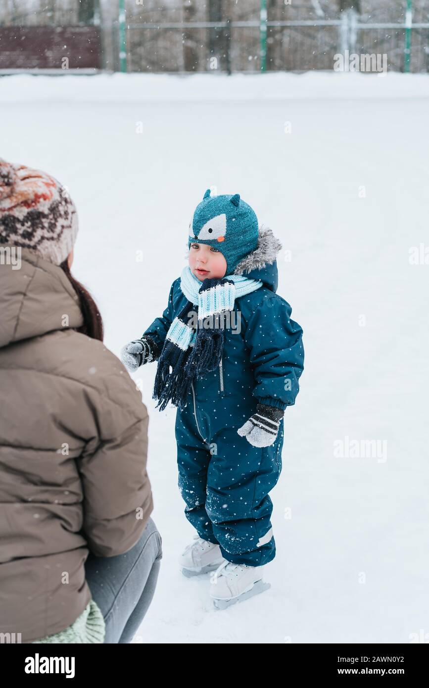 Piccolo ragazzo divertente che impara a pattinare con la madre nel parco. All'aperto. Sport invernali Foto Stock