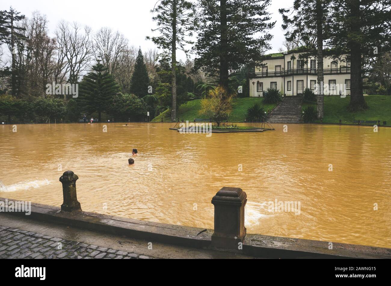 Furnas, Azzorre, Portogallo - 13 gennaio 2020: Piscina termale con acqua calda di ferro nel Giardino Terra nostra. Persone che nuotano in acqua di colore marrone da una sorgente vulcanica. Attrazione turistica portoghese. Foto Stock
