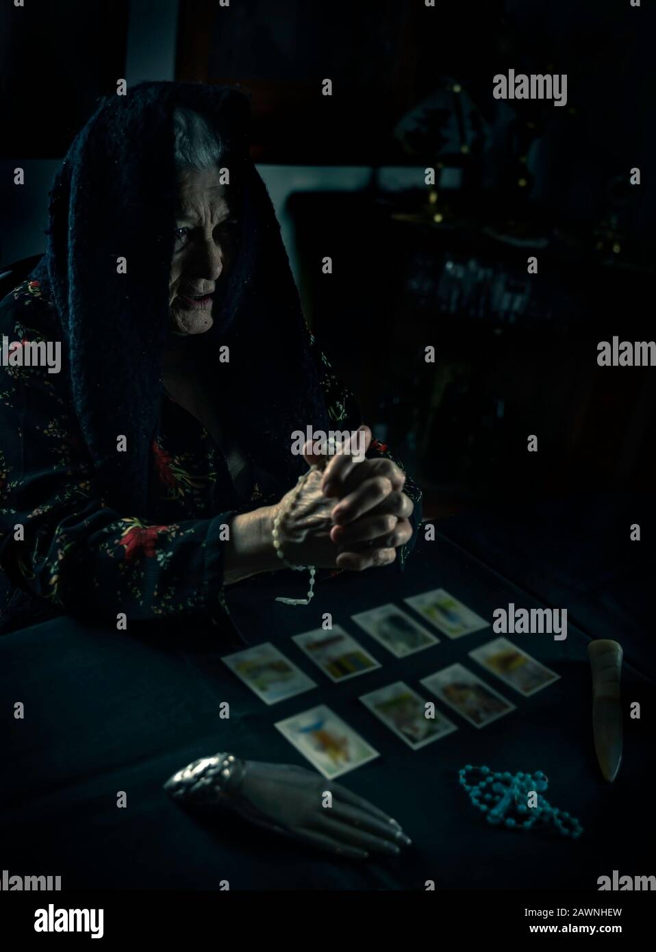 Una vecchia donna che prega sopra le carte tarocchi. Vecchie mani rughe. Concetto occulto di narrazione di fortuna. Sfondo mistico scuro. Foto Stock
