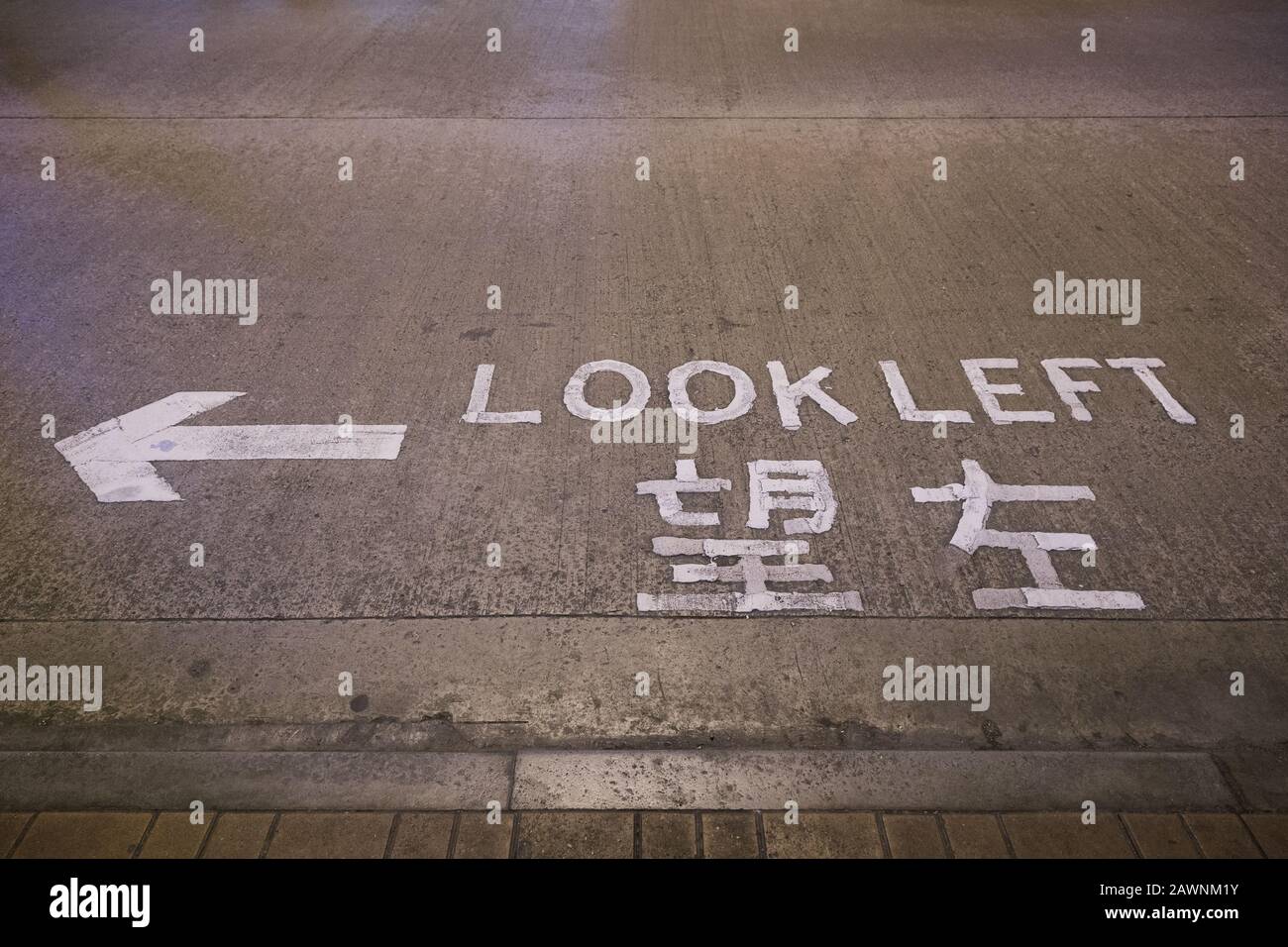 Freccia e 'guardare a sinistra' attenzione o segno scritto in inglese e cinese su una strada a Hong Kong, Cina. Foto Stock