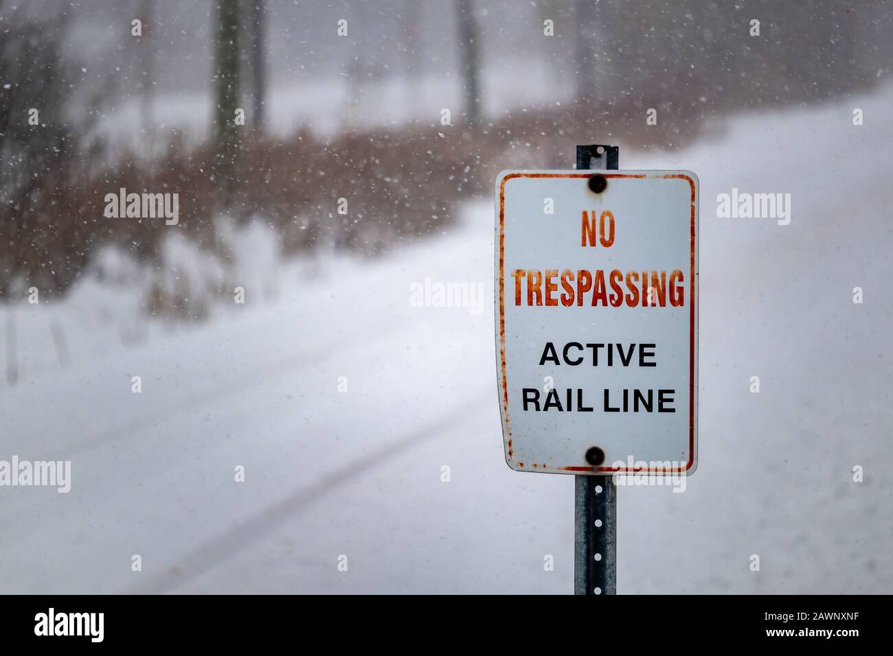 In inverno, in una giornata innevata, un cartello posto all'incrocio dei binari ferroviari e un sentiero legge: "No Tressprassing: Active Rail Line". Foto Stock