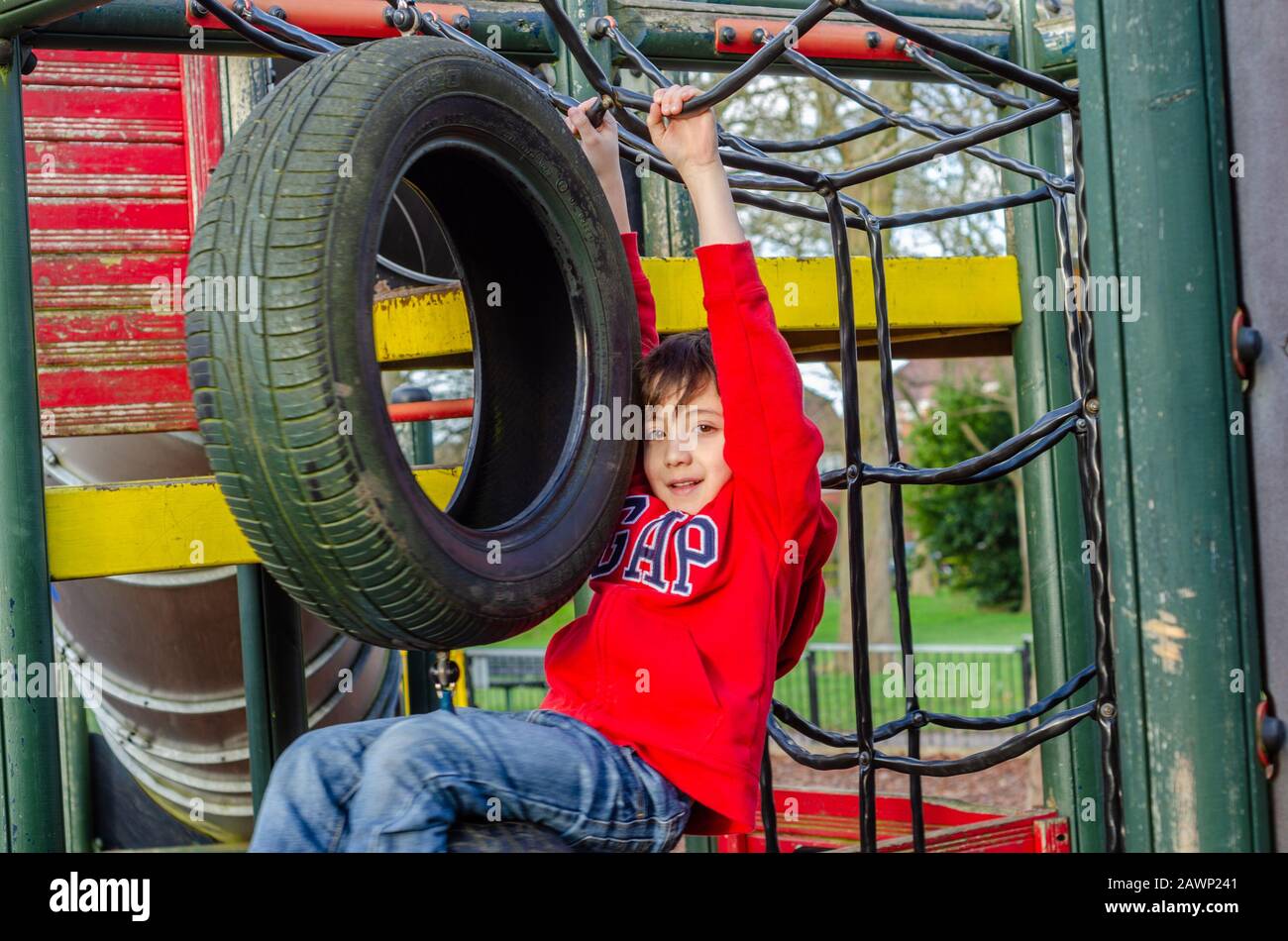 Un ragazzo felice di giocare su una cornice di arrampicata in un parco giochi per bambini. Foto Stock