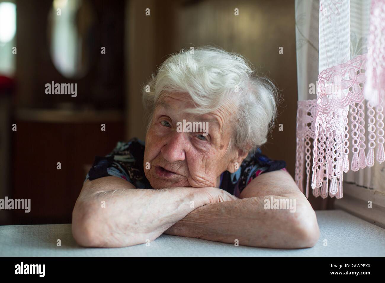 Una vecchia donna siede pensierosamente al tavolo. Foto Stock