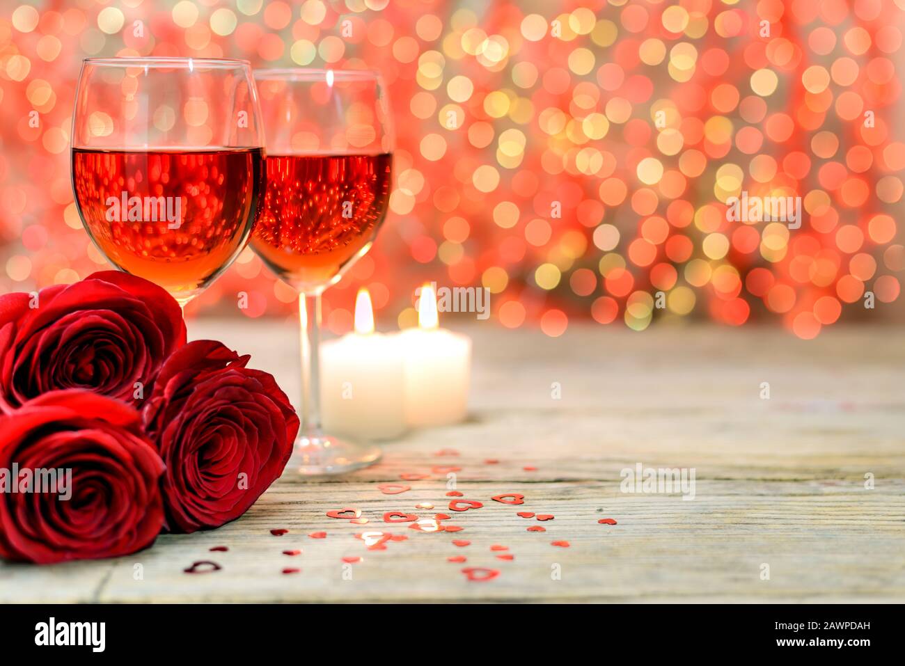 Concetto di San Valentino. Due bicchieri di vino, rose rosse e candele accese su un vecchio tavolo di legno davanti a uno sfondo luminoso sfocato con copia Foto Stock