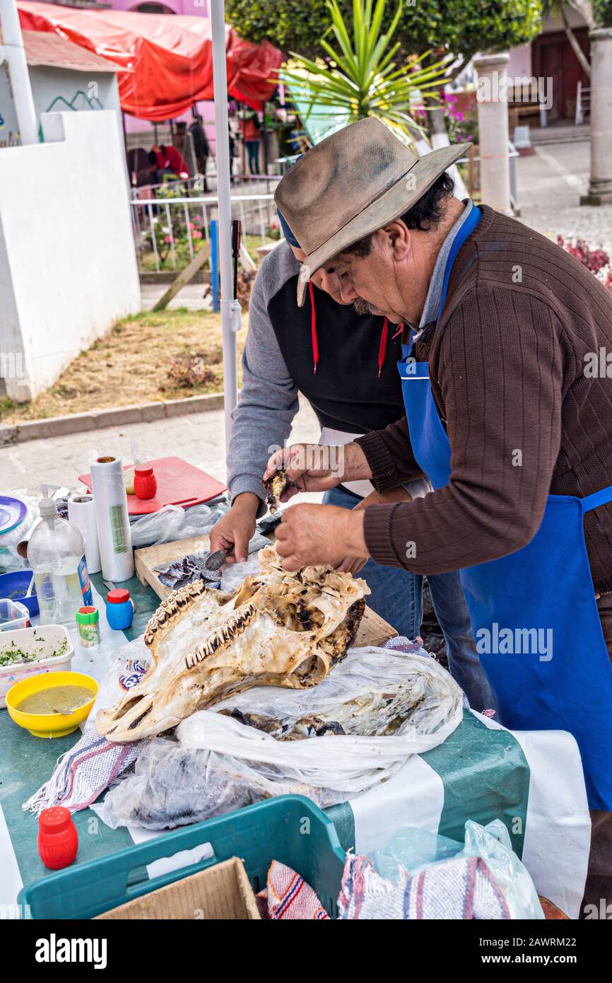 Un venditore prepara tacos fatti con carne di guancia di manzo fuori un cranio di mucca sulla Plaza de la Constitucion in Angangugueo, Michoacan, Messico. Angangugueo è una piccola e remota cittadina di montagna e il punto di ingresso al Santuario delle farfalle di Sierra Chinccua Monarch. Foto Stock