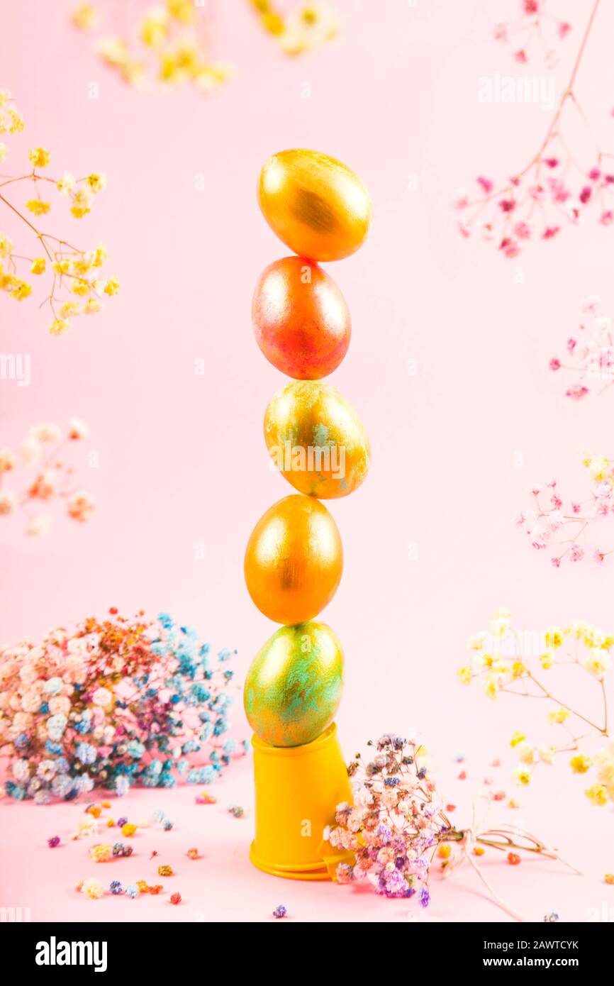 Le uova di Pasqua dipinte sono disposte in una torre verticale e si equilibrano su uno sfondo rosa tra i fiori. Concetto creativo di pasqua. Foto Stock