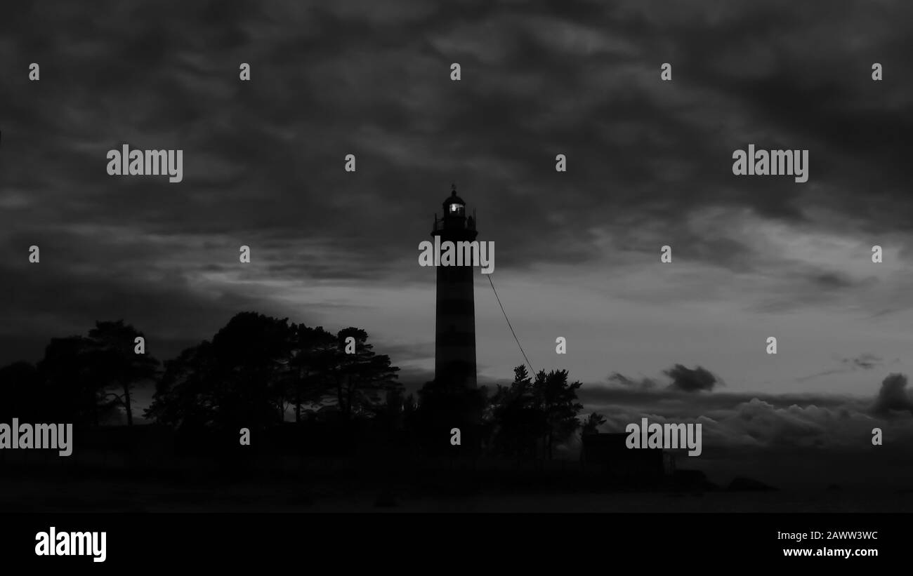 La torre faro risplende al buio con un cielo spettacolare. Silhouette di faro luminoso nelle tenebre Foto Stock